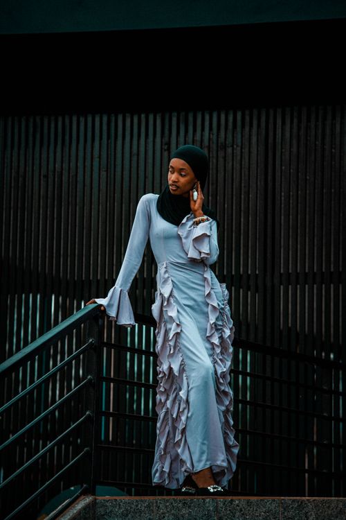 Free Portrait of an elegant woman in a ruffled dress leaning on a railing, showcasing urban fashion. Stock Photo