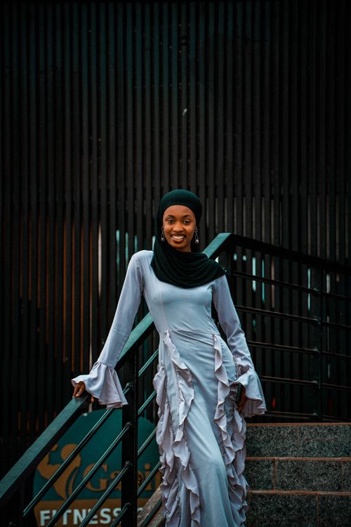 Free Smiling woman in a stylish traditional dress stands on outdoor stairs, showcasing cultural elegance. Stock Photo