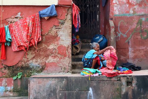 Free An elderly woman sorts colorful clothes on an urban street, showcasing daily life. Stock Photo