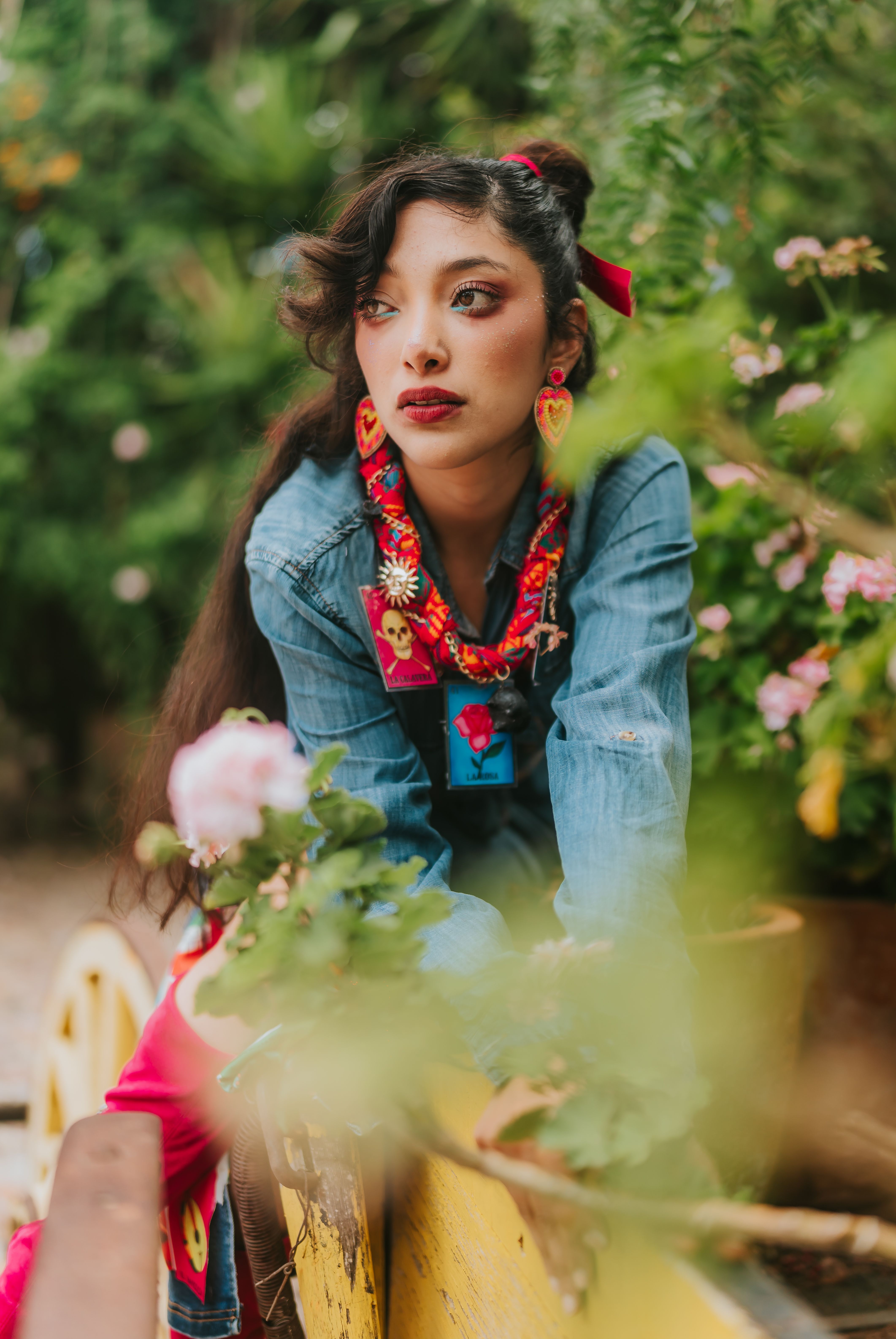 A young woman in a colorful floral scarf poses in a lush garden, exuding a vibrant and natural style.