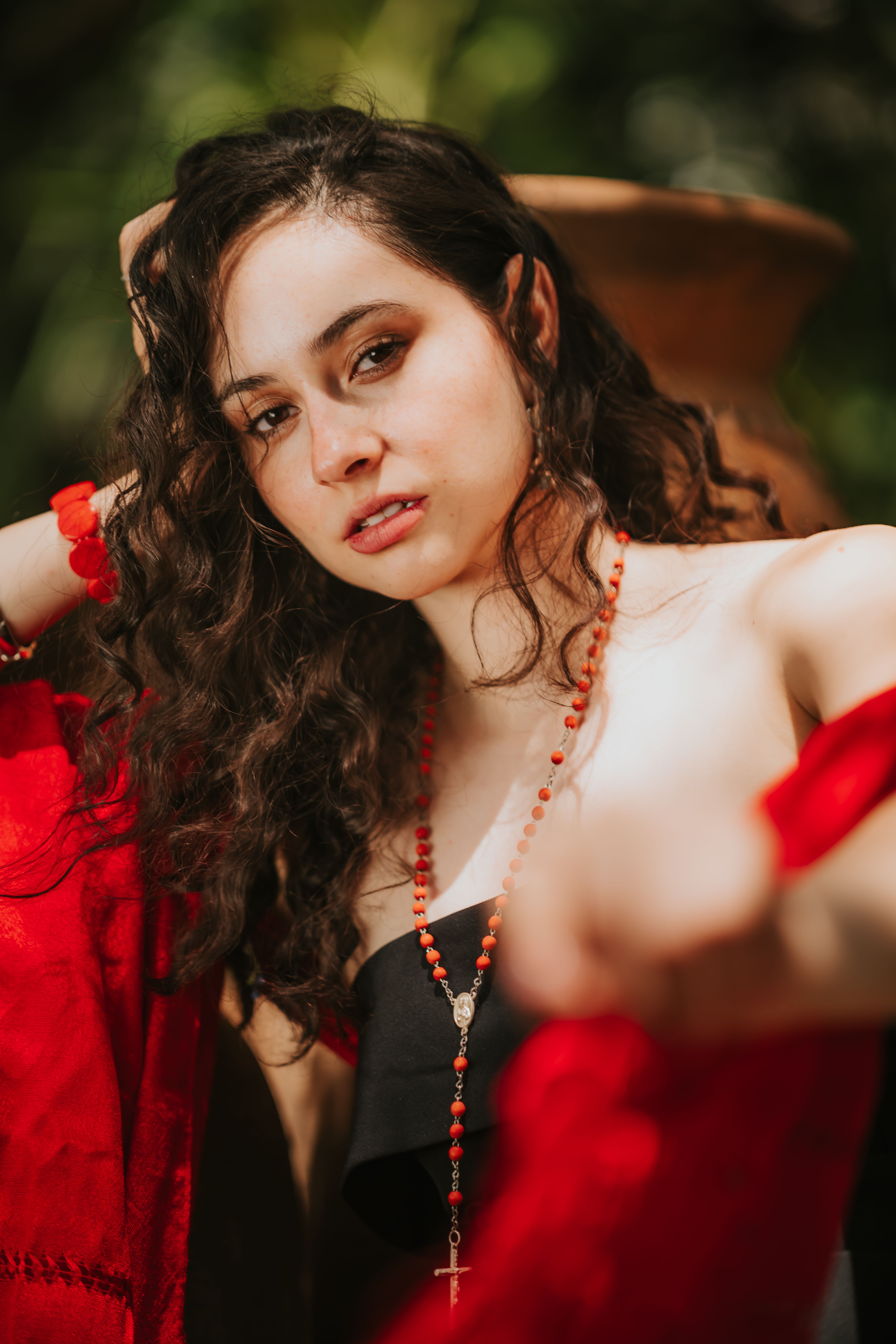 Intimate portrait of a woman with curly hair and red accessories in an outdoor setting.