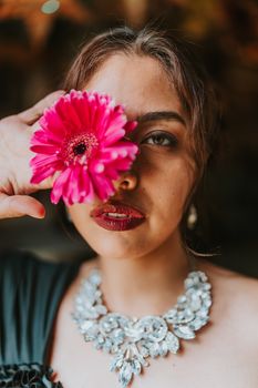 Close-up portrait of woman holding a pink gerbera daisy with elegant jewelry.
