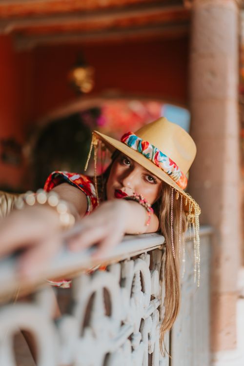 Free Elegant woman in colorful hat and dress relaxing on a balcony in a tropical resort. Stock Photo
