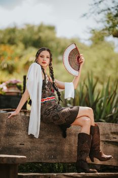 A woman in traditional attire holding a fan while sitting outdoors.