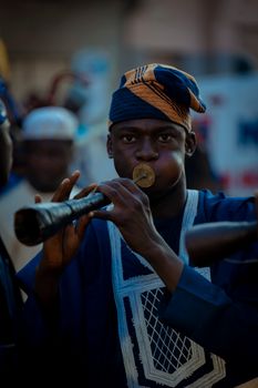 A musician in vibrant attire plays a traditional African flute at an outdoor event.