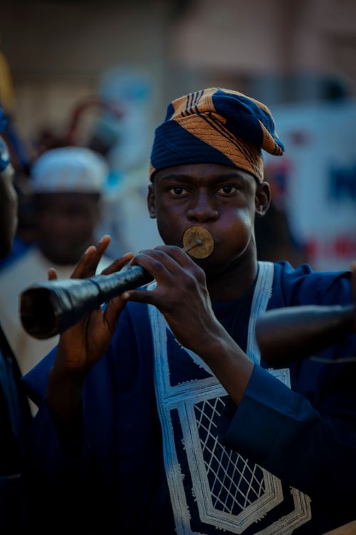 Free A musician in vibrant attire plays a traditional African flute at an outdoor event. Stock Photo