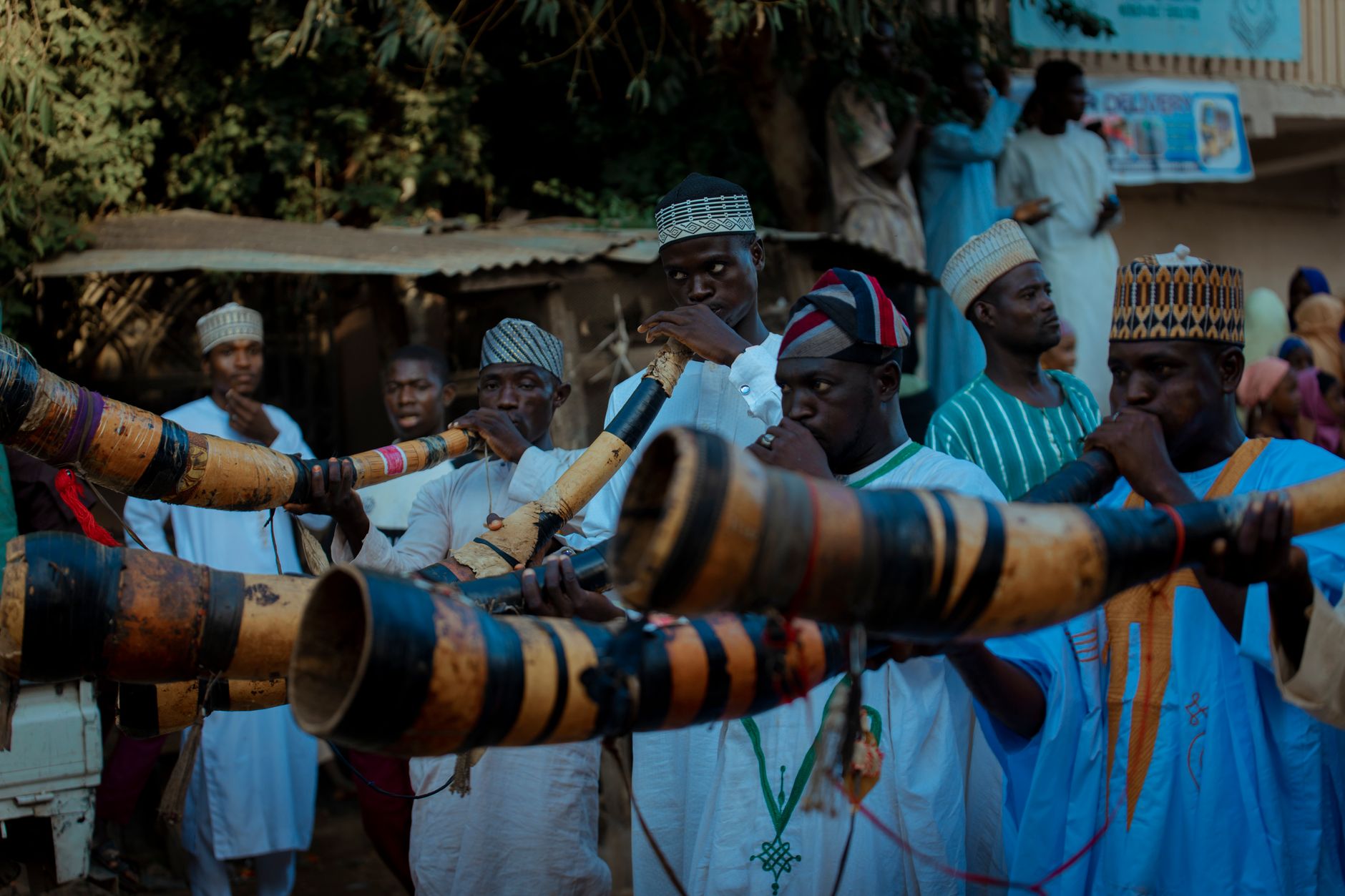 A group of men in traditional attire playing wooden horns at a cultural event outdoors.