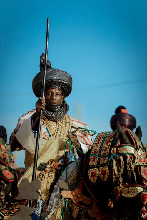 Free A traditional Tuareg horseman wearing ornate clothing and turban in a desert setting under clear skies. Stock Photo