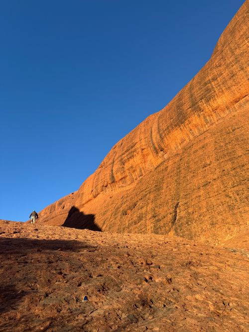 Free A lone hiker traverses the rugged terrain of Uluru in Australia's Northern Territory against a bright blue sky. Stock Photo