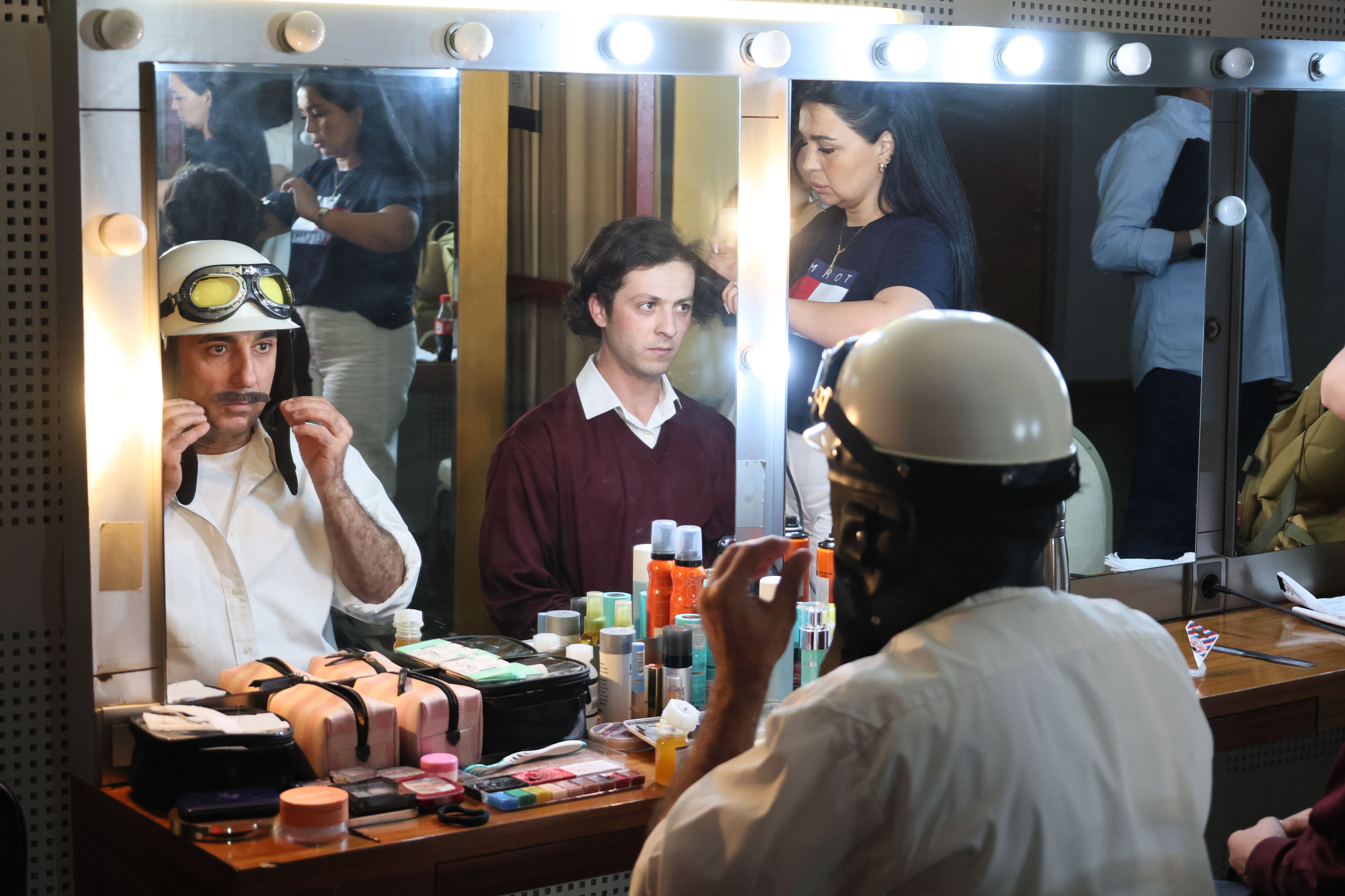 Actors preparing with makeup artists in a theatre dressing room, creating theatrical characters.