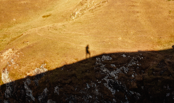 Shadow of a person on a rocky cliff captured during golden hour, highlighting grassland.