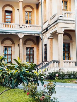 A beautiful historic building with arched windows, surrounded by a lush garden with blooming flowers.