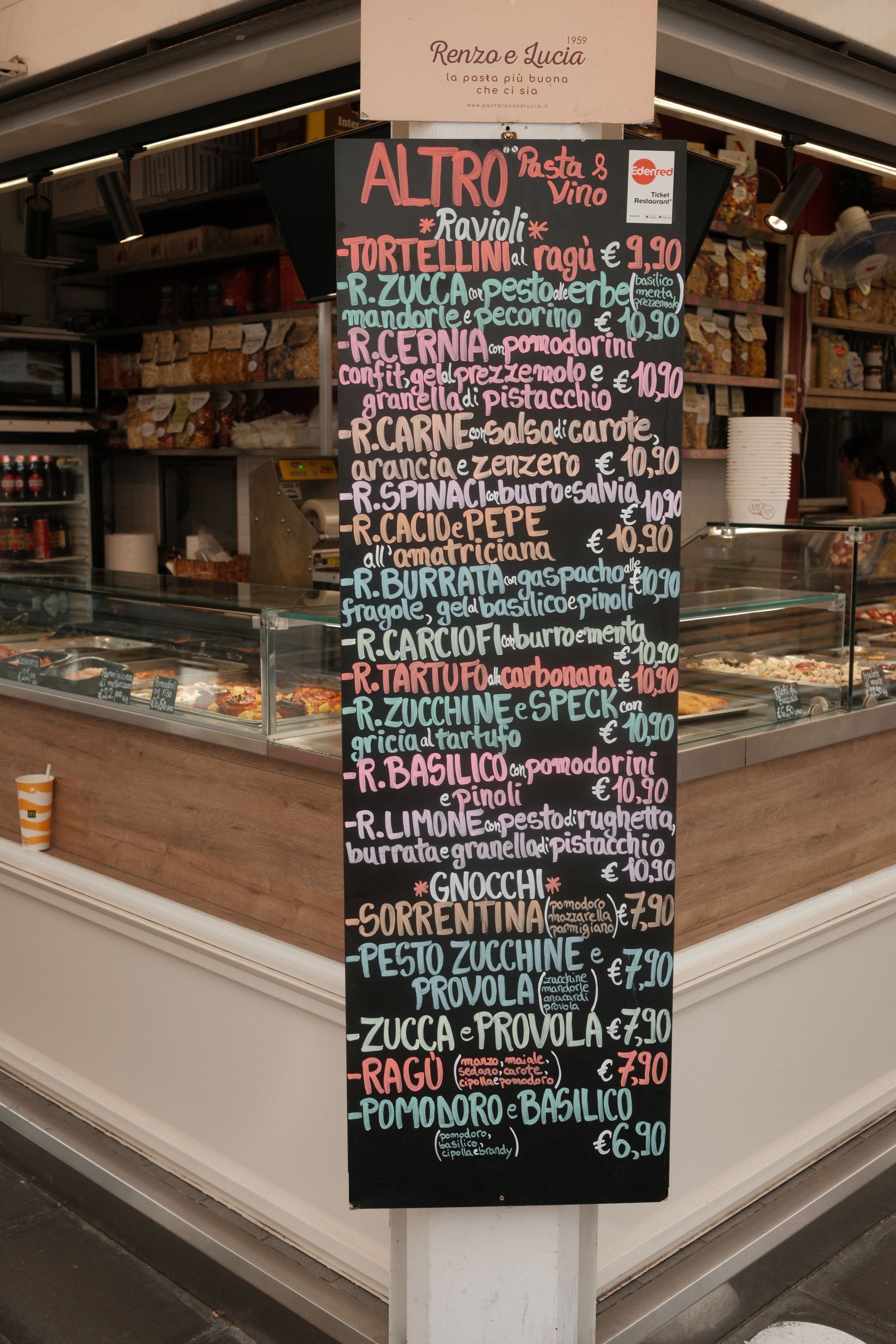 Lavagna con menu di piatti di pasta italiana e prezzi in un locale.
