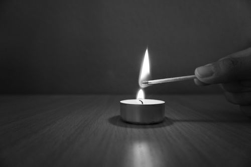 Free A serene black and white image of a hand lighting a tealight candle with a matchstick. Stock Photo