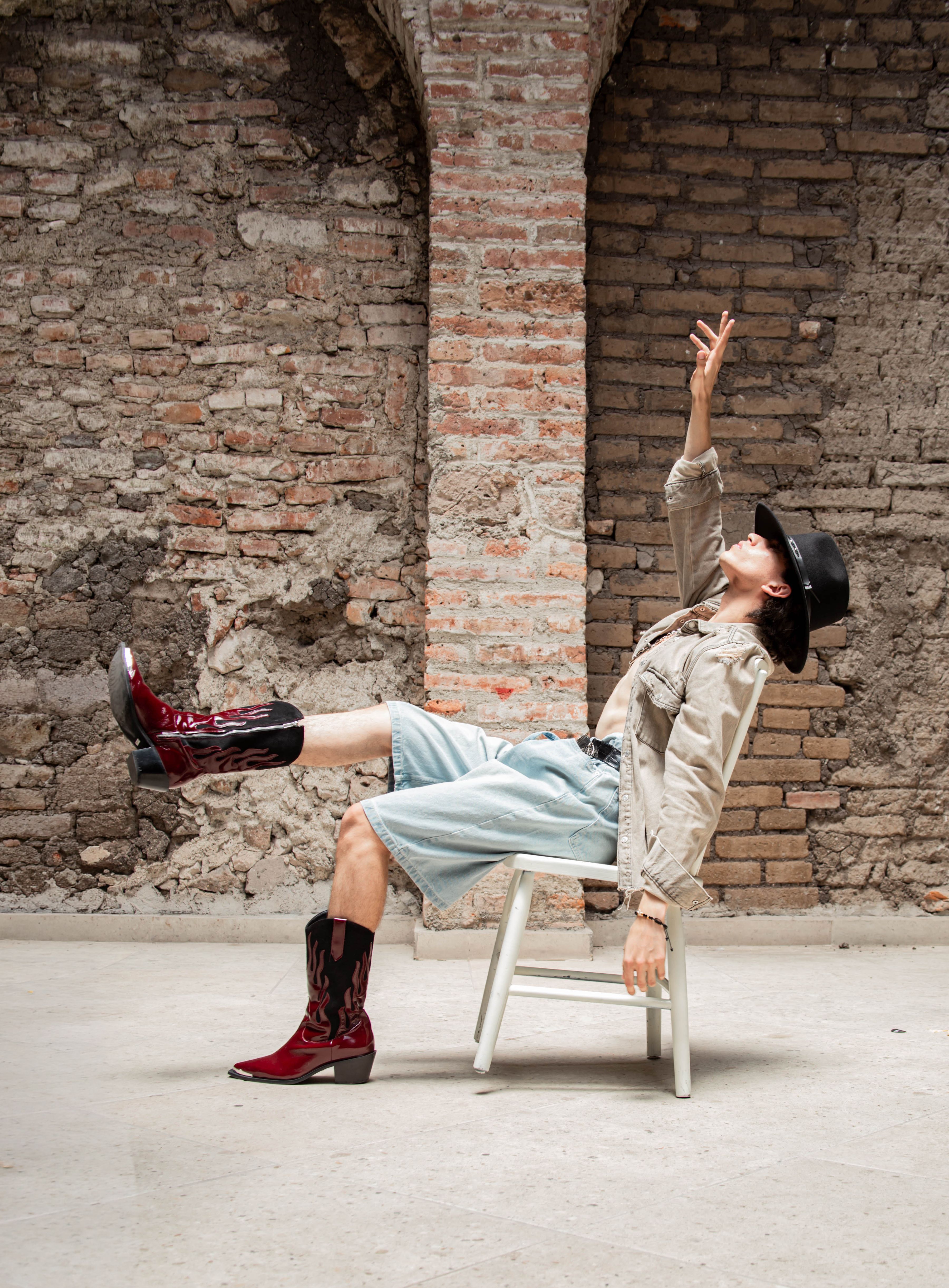 Chic individual in cowboy attire striking a creative pose against a rustic brick wall in León, Mexico.