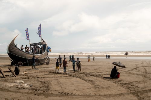 Free A traditional fishing boat on a sandy beach with people enjoying a day by the sea. Stock Photo