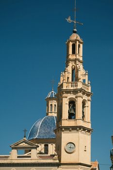 Gothic bell tower with a clock and blue dome under a vibrant blue sky in Planes, Spain.