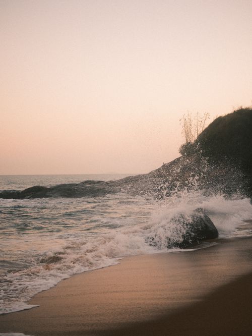 Free Gentle waves crash against the rocky shore under a pastel sunset sky, creating a serene coastal scene. Stock Photo