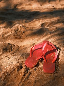 Bright red flip flops on sunlit sandy beach, conveying summer vacation vibes.