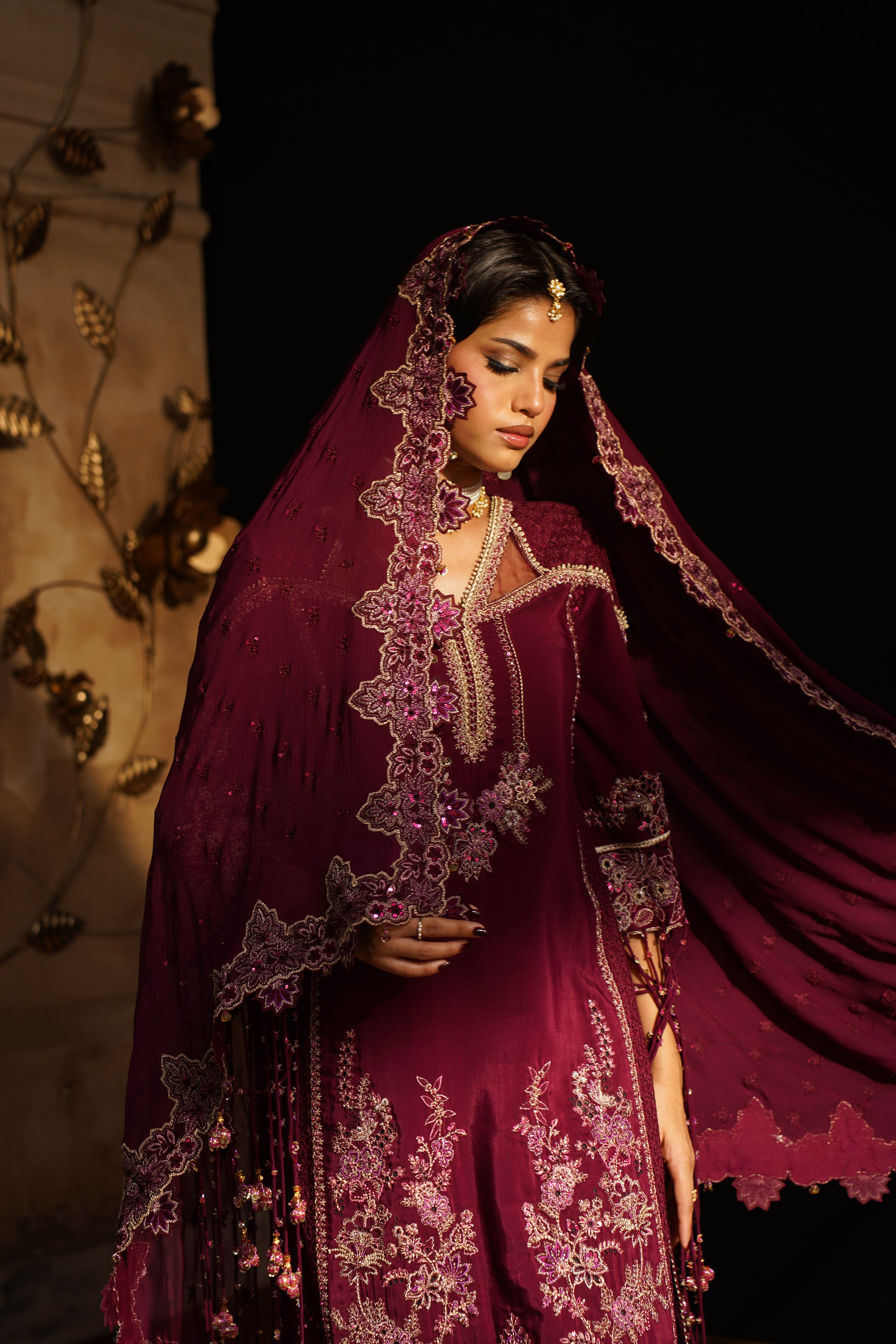 A woman in maroon velvet with an embroidered dupatta over her head