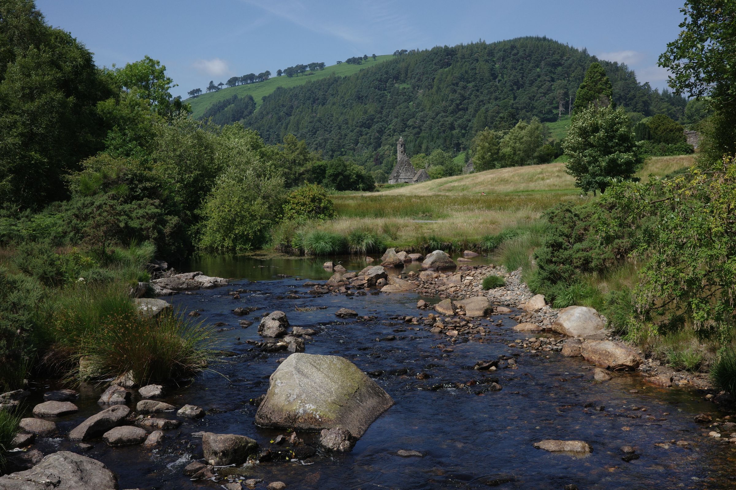 A stream flows through greenery in the Irish countryside under a blue sky