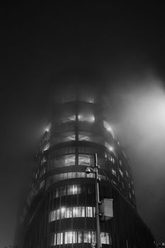 Eerie black and white view of a foggy urban building at night, illuminated softly.