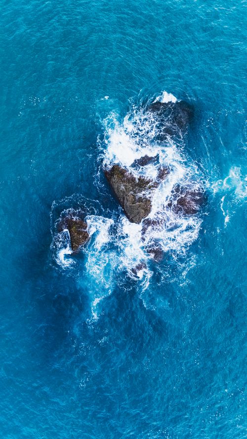 Free Stunning aerial shot of ocean waves crashing onto rocks, showcasing the power of nature. Stock Photo
