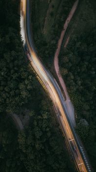 Captivating aerial view of a winding road with car light trails through a dense forest at night.