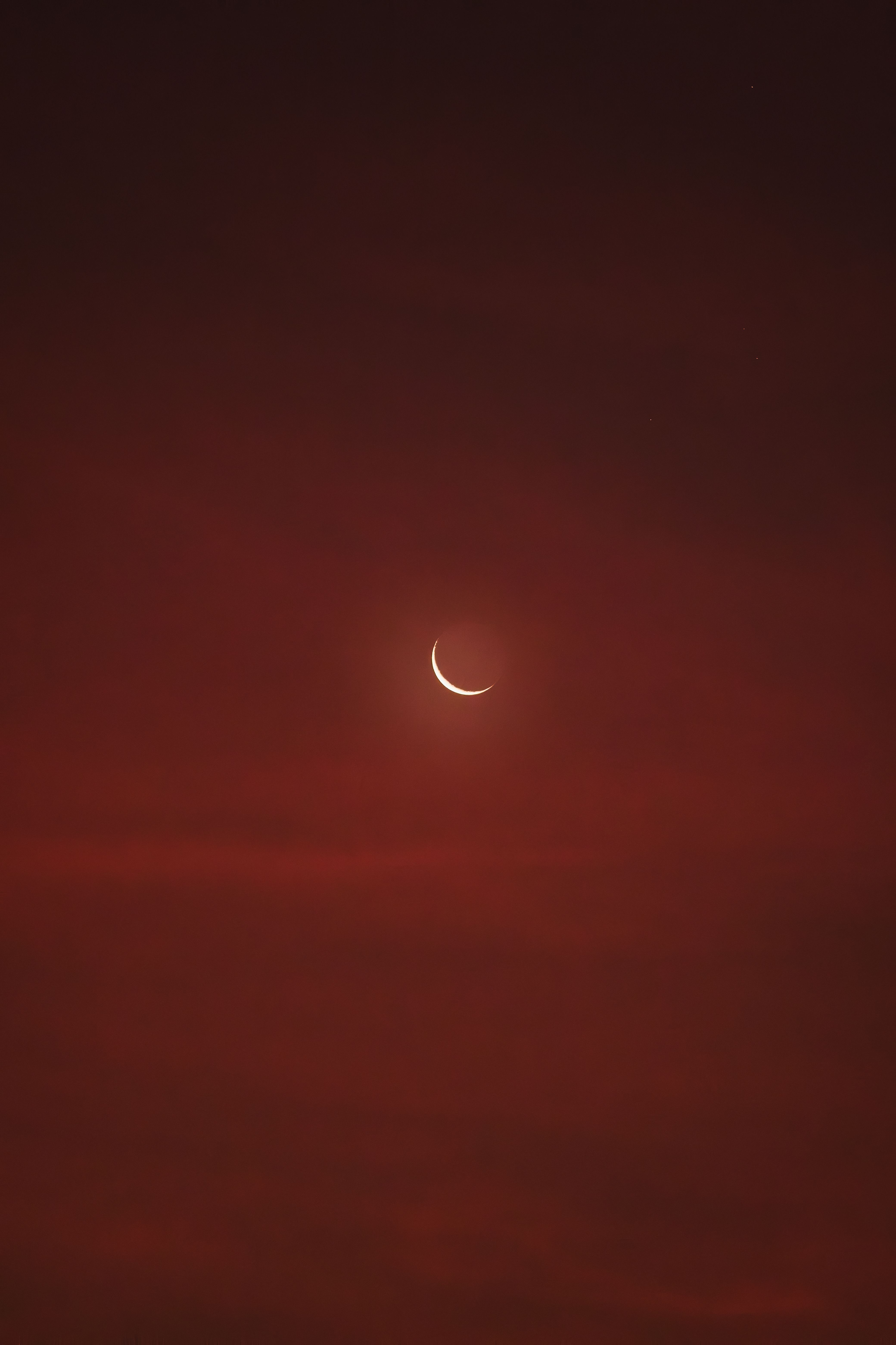 A serene crescent moon glowing against a rich red twilight sky, evoking a calm and mystical night scene.
