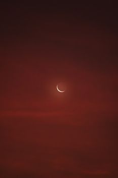 A serene crescent moon glowing against a rich red twilight sky, evoking a calm and mystical night scene.