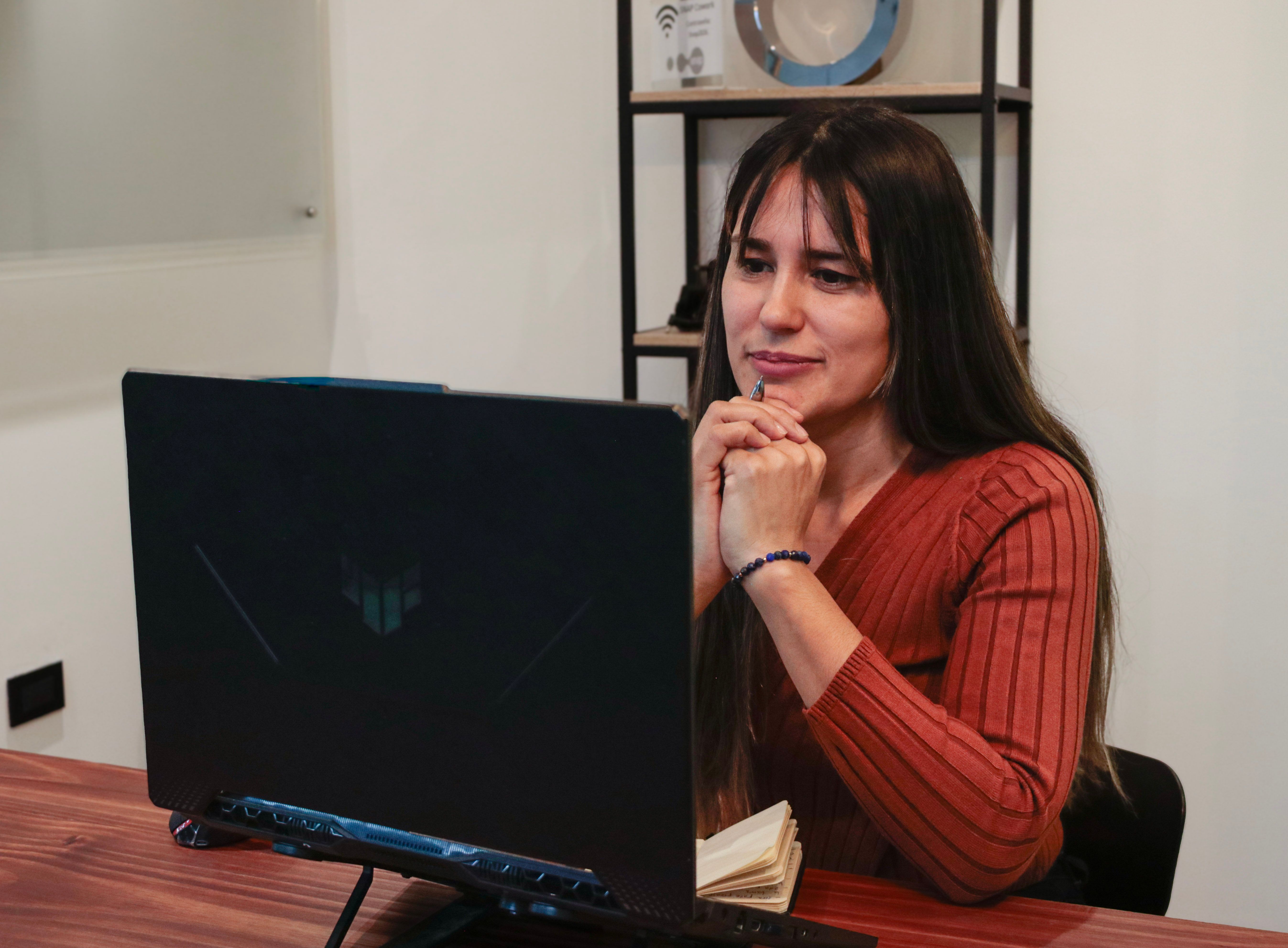 Eine Frau, die auf den Bildschirm eines Laptops schaut, die Hände unter dem Kinn zusammengeführt.