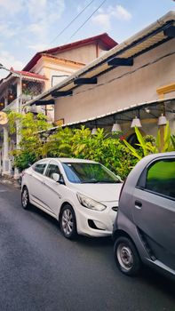Charming street in Goa, India with parked cars and lush greenery, showcasing a vibrant neighborhood.