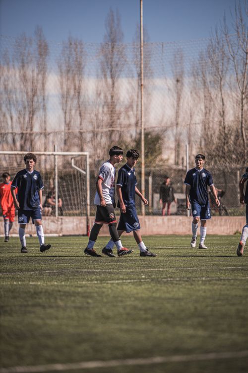Free Teenagers playing soccer on a sunny outdoor field with sparse trees in the background. Stock Photo