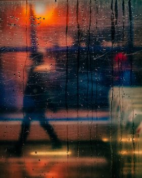 Blurry silhouette of a person walking behind a rain-streaked glass at night in Warsaw.