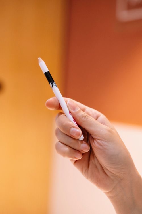 Free Close-up of a hand holding a white marker pen against an orange background, perfect for office or creative themes. Stock Photo
