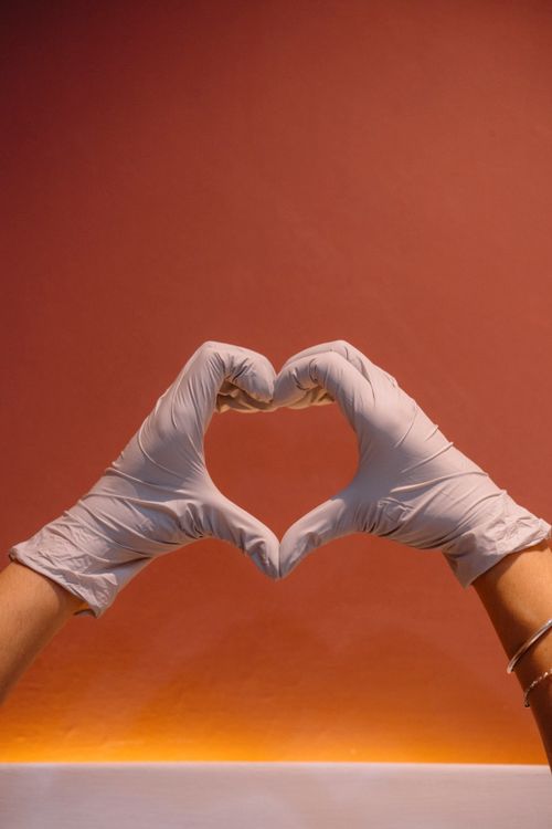 Free Hands in gloves forming a heart shape against warm orange backdrop, symbolizing healthcare and compassion. Stock Photo