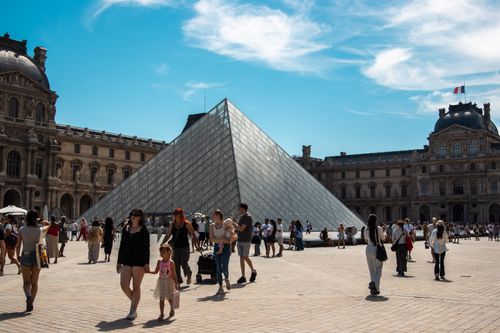 Free Tourists gather at the Louvre Pyramid in Paris under a clear blue sky. Stock Photo
