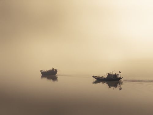 Free Two fishing boats navigate a calm, misty waterway at sunrise, casting reflections. Stock Photo
