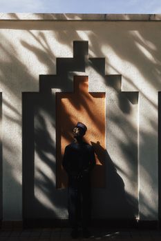 A man stands in front of a patterned wall in Nigeria, casting shadows under soft sunlight.