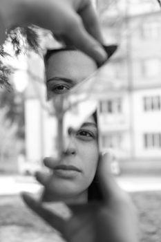 Black and white portrait of a woman's face reflected in fractured mirror pieces outdoors.