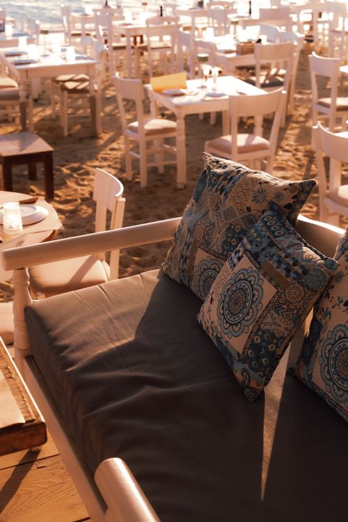 Free Relaxing beach dining setup at sunset on Naxos, Greece, featuring elegant seating and decorative pillows. Stock Photo