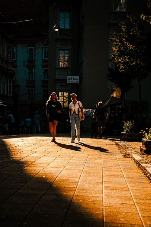 Free A vibrant street scene during sunset with three people walking, casting long shadows. Stock Photo