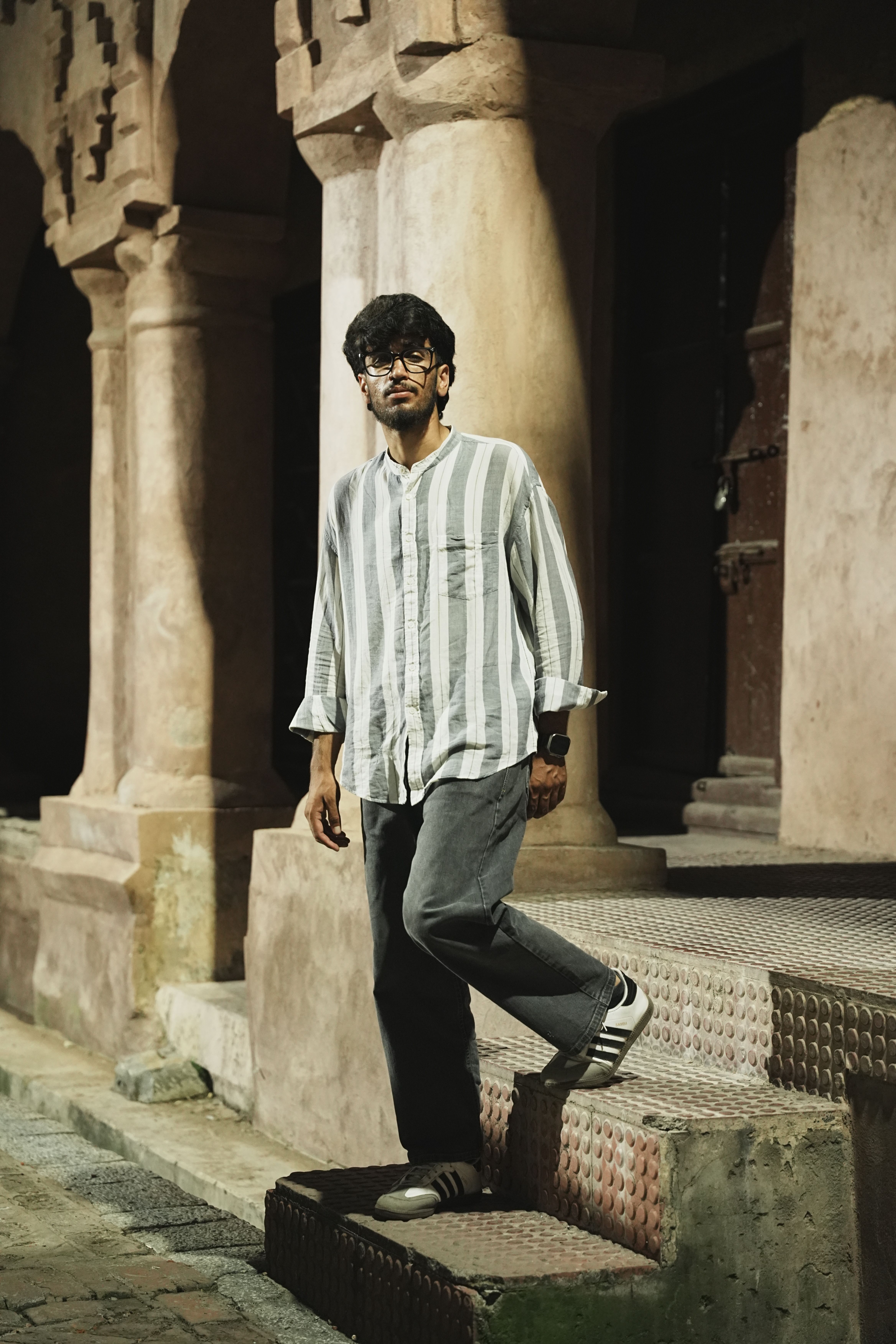 Adult man in casual attire stands by a historic building at night, capturing a serene and thoughtful mood.