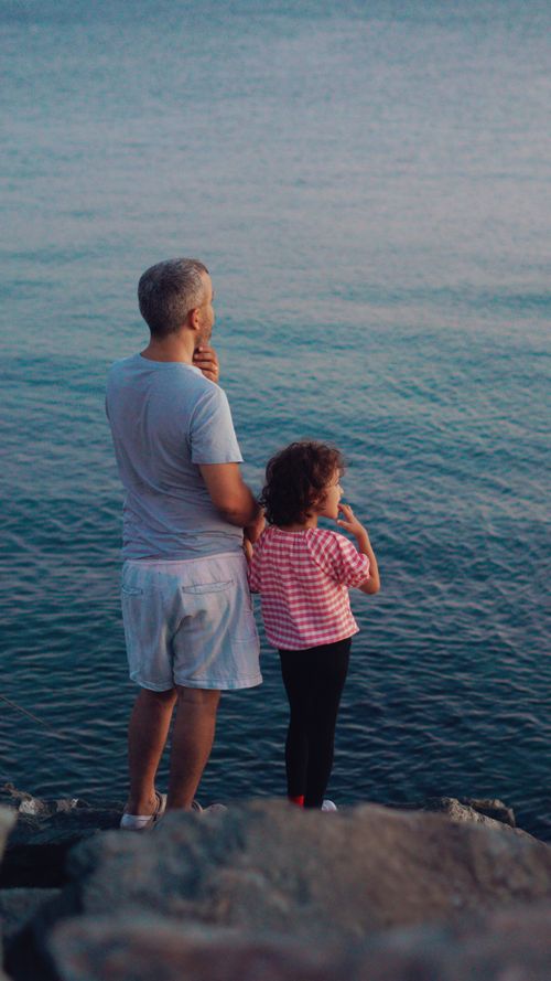Free A touching moment between a father and child gazing at the sea, representing familial bonding and tranquility. Stock Photo