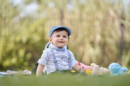 Free Cute baby boy wearing a cap and suspenders, enjoying a sunny day outdoors. Stock Photo
