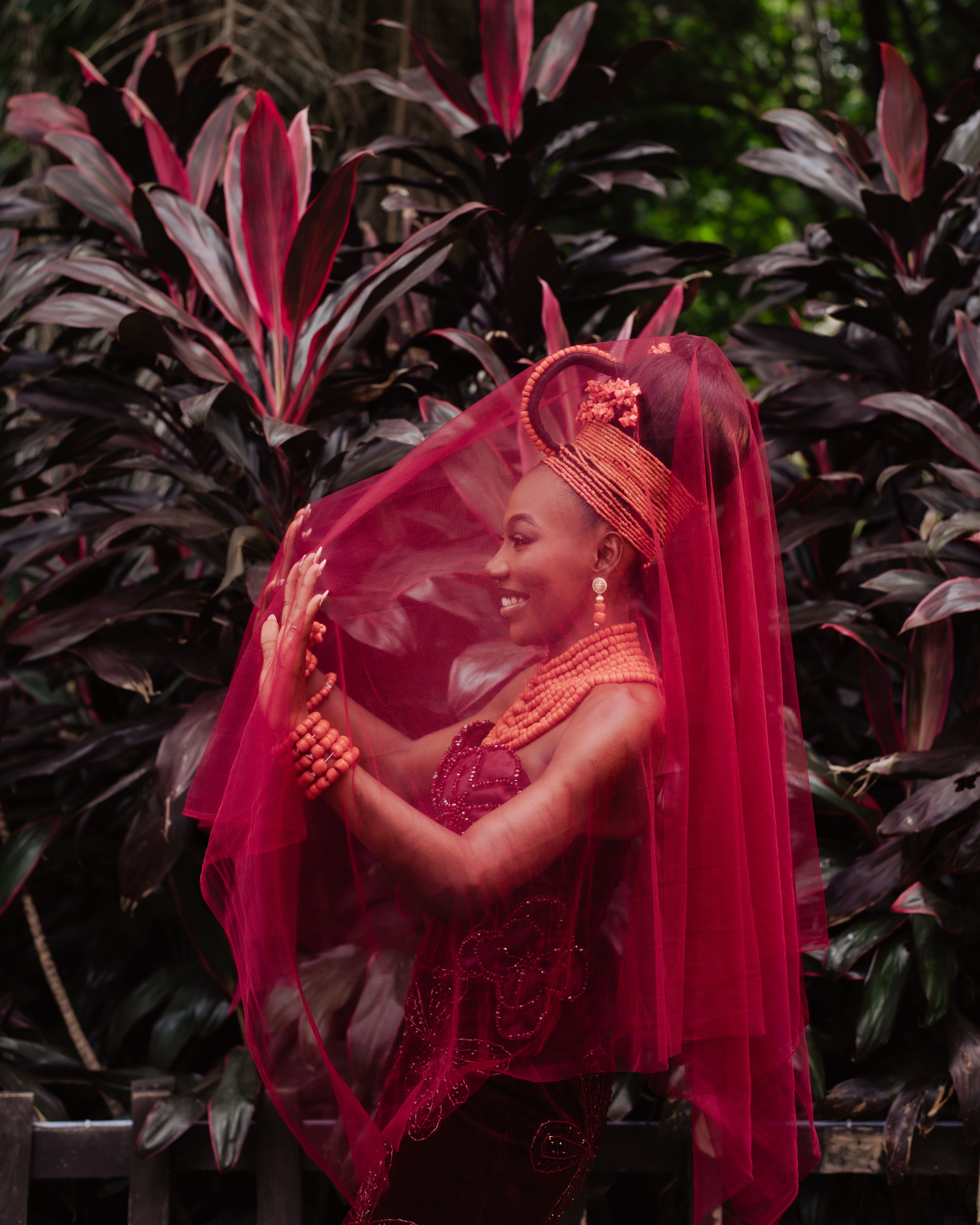 Vibrant Nigerian bride in traditional attire surrounded by lush foliage.