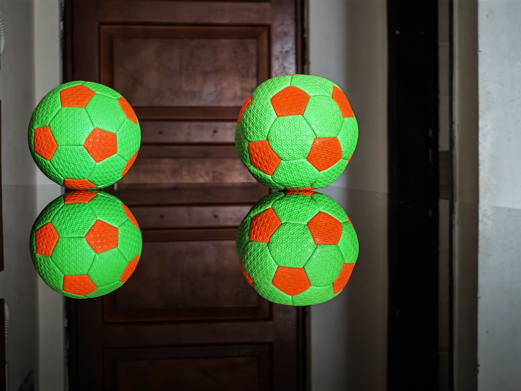 Dua bola sepak berwarna cerah terpantul di permukaan mengkilap di dalam ruangan.
