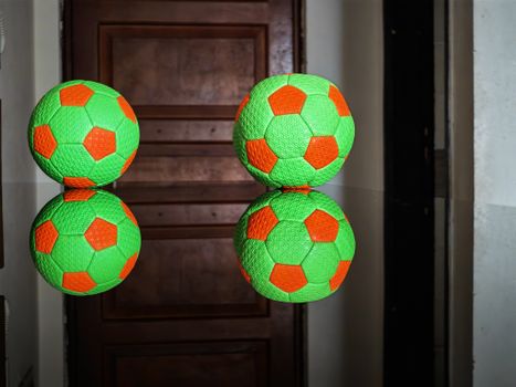 Two vibrant soccer balls reflected on a shiny surface indoors.