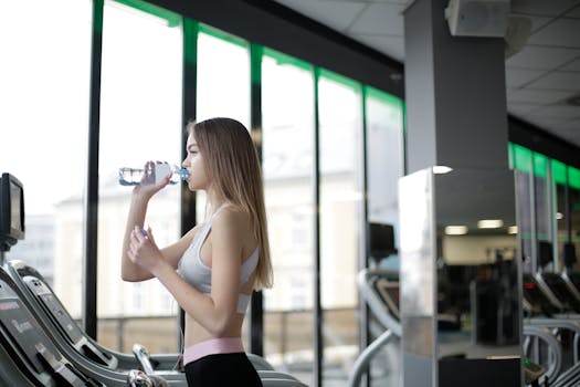 A young woman drinks water during her workout on a treadmill at a modern indoor gym.