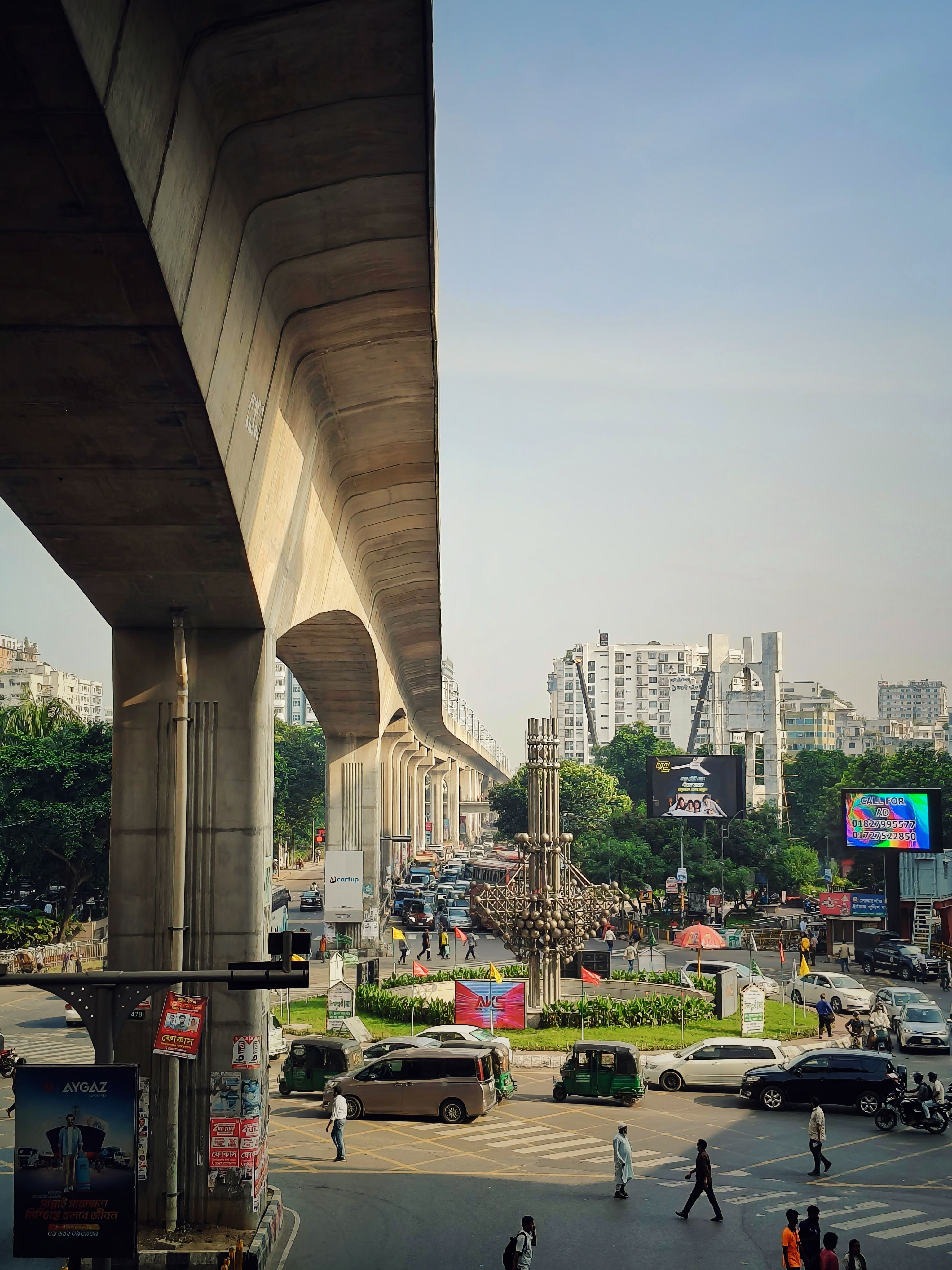 A bustling city intersection with elevated railway, highways, and urban structures under a clear blue sky.